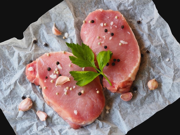 生のポークチョップステーキは、食べ物や料理のために野菜とスパイスを使って木製のまな板で準備します