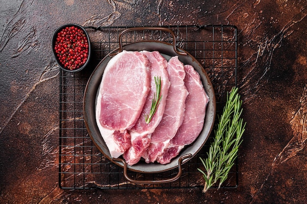 Raw pork chop steaks in steel tray with rosemary Dark background Top view