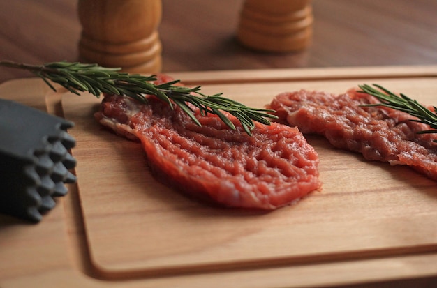 Raw pork chop with seasonings and a sprig of rosemary on a wooden board