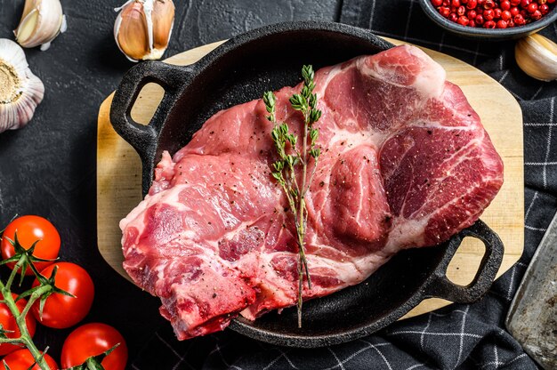 Raw pork cutlet steak in a pan. Piece of raw meat ready for preparation with greens and spices.  Black background. .