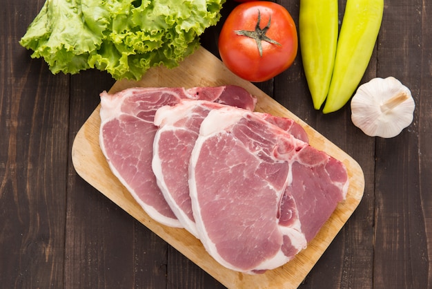 Raw pork on cutting board and vegetables on wooden table