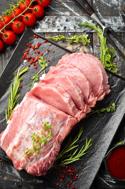 Raw pork fillet with spices on a black stone background. Meat. Top view. Rustic style.