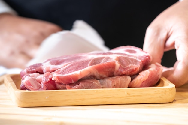 Raw Pork is prepared for Cook It is on wood plate in studio light with Chef hand background