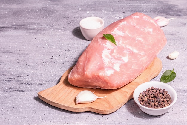 Raw pork loin on a chopping board. Fresh meat, spices, sea salt, leaves. Modern hard light, dark shadow. Grey stone concrete background, copy space