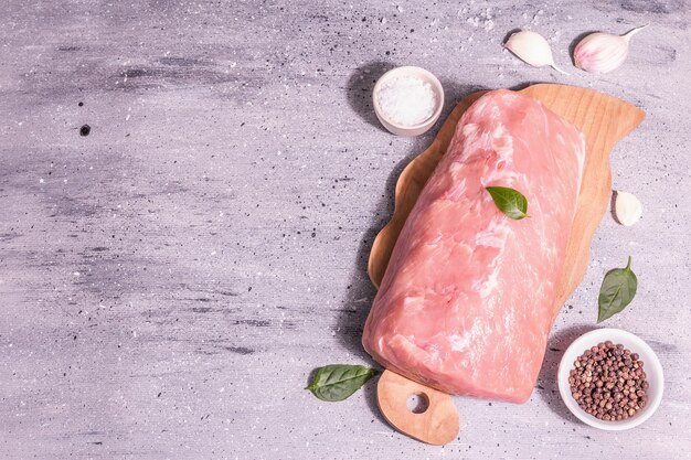 Raw pork loin on a chopping board. Fresh meat, spices, sea salt, leaves. Modern hard light, dark shadow. Grey stone concrete background, top view