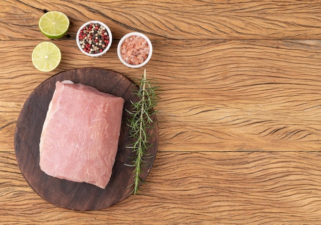 Raw pork loin meat over wooden board with seasonings and copy space.