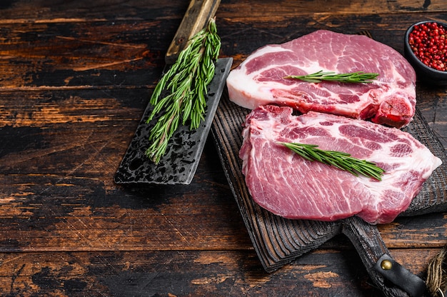 Сырые стейки из свиной корейки с зеленью на разделочной доске с ножом для мяса