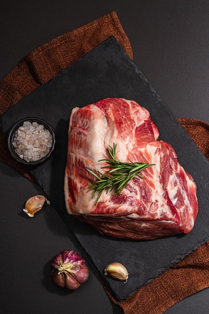 Raw pork loin with spices and herbs Fresh meat cut ingredient for cooking protein food healthy food lifestyle Trendy hard light dark shadow black stone concrete background top view