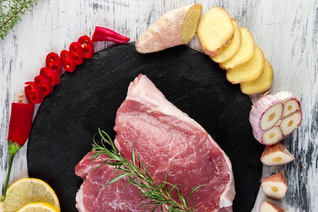 Raw pork meat on black slate plate with spice ingredient - rosemary, ginger, chilli pepper, onion.Top view. Flat lay. Copy space.