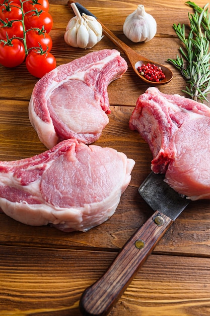 Raw pork meat chopes with herbs and spices with meat american cleaver on wooden background side view vertical.