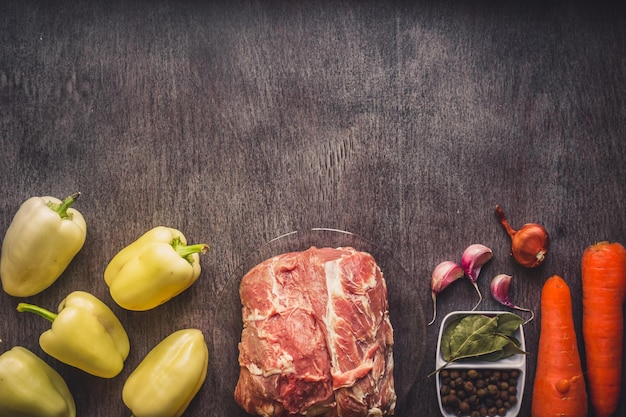 Raw pork meat on a dark wooden surface and ingredients for cooking. Food background with copy space. Toned