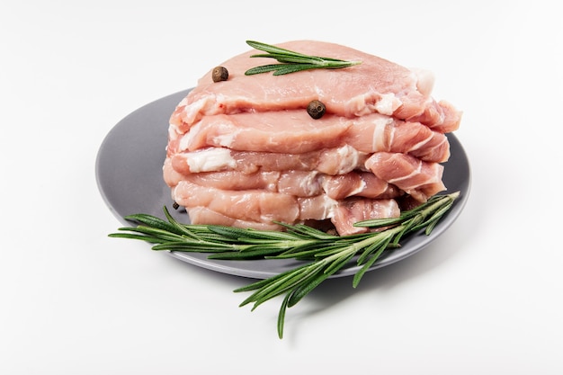 Raw pork meat on the plate with rosemary, salt and pepper.