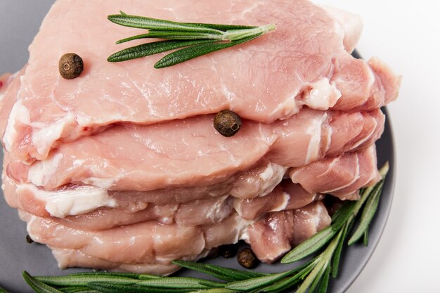 Raw pork meat on the plate with rosemary, salt and pepper.