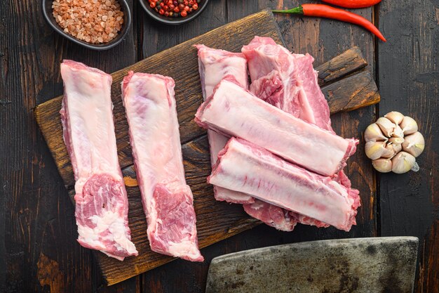 Costolette di carne di maiale cruda con ingredienti per set da cucina, con il vecchio coltello da macellaio mannaia, sul vecchio tavolo in legno scuro, vista dall'alto laici piatta