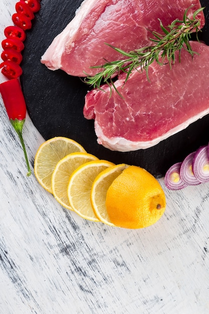 Raw pork meat Tenderloin on black slate plate with spice ingredient - rosemary, ginger, chilli pepper, onion.Top view. Flat lay. Copy space.