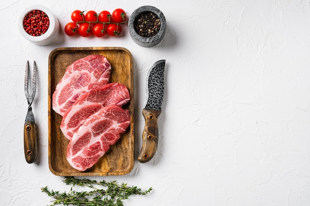 Raw pork neck cut steak set, on white stone table background, top view flat lay, with copy space for text