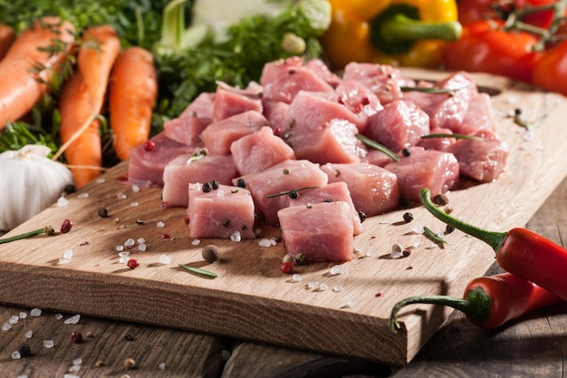 Фото Сырая свинина на разделочной доске и свежие овощи на деревянном столе