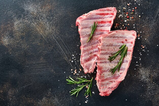 Raw pork ribs or fresh uncooked meat with spices on black wooden tray with paprika, garlic cloves and herbs. Dark textured background with copy space for text.