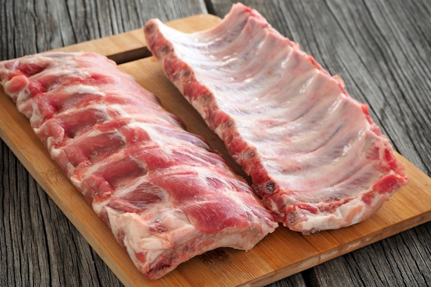 Raw pork ribs for grilling or roasting on a cutting board on an old wooden table.