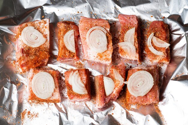 Raw pork ribs with raw onions lie on foil ready to be baked in the oven