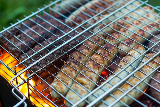 Raw pork sausages roasted on the grill, barbecue season outdoors. Meat roasting at barbecue. 
