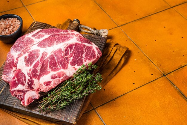 Raw pork steak chops neck meat with herbs orange background top view copy space