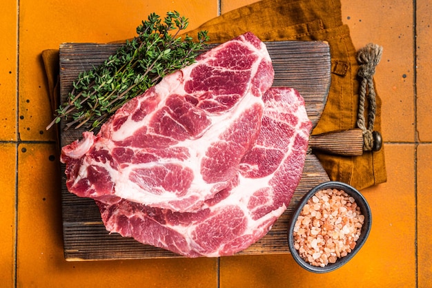 Raw pork steak chops neck meat with herbs orange background top view