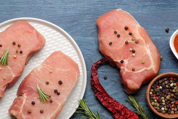 Raw pork steak on a plate, meat and ingredients for cooking, spices herbs and vegetables on a light background. top view