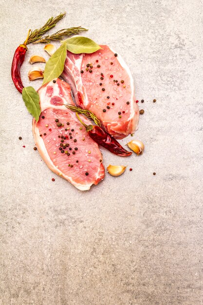 Raw pork steak with spices and dried herbs. Salt, garlic, hot pepper, rosemary, bay leaf on a stone background, top view.