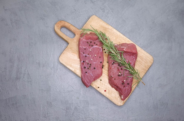 Raw pork steak with spices and herbs on wooden cutting board