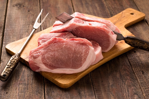 Raw pork steaks on cutting board knife and fork for cutting meat