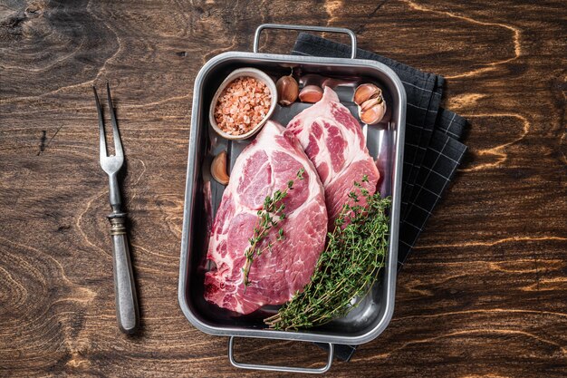 塩とタイムを添えたキッチントレイの新鮮な首肉からの生のポークステーキ。木製の背景。上面図。