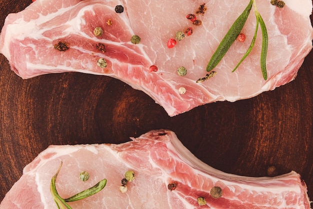 Raw pork steaks with rosemary and pepper on a clay plate closeup Top view Flat lay