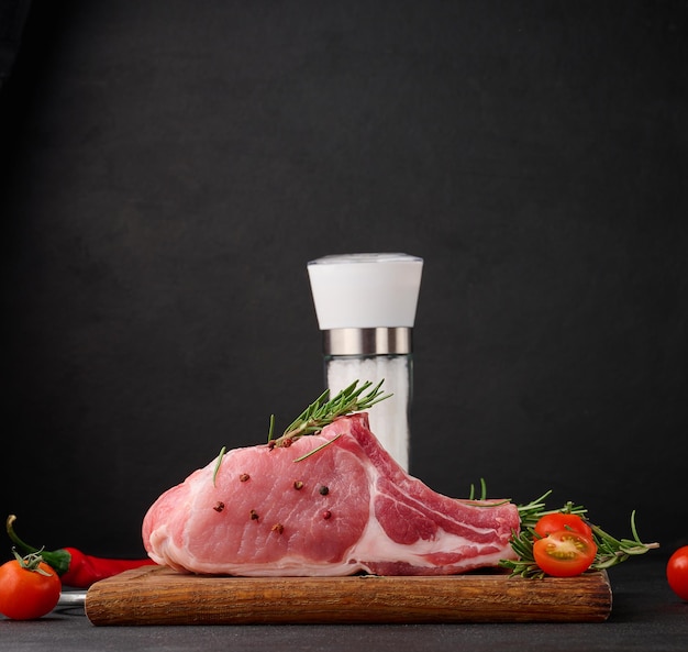 Filetto di maiale crudo sull'osso e spezie su un tagliere di legno su sfondo nero porzione per pranzo e cena