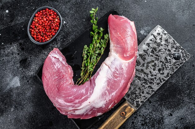 Raw pork tenderloin meat on a marble board. Black background. Top view.