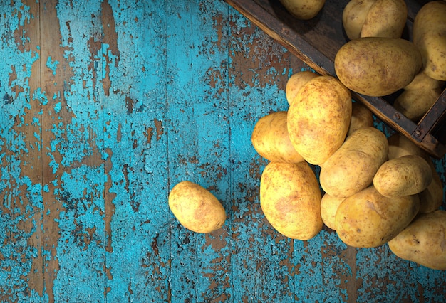 Foto alimento di patate crude. patate e una vecchia scatola su una tavola di legno blu.