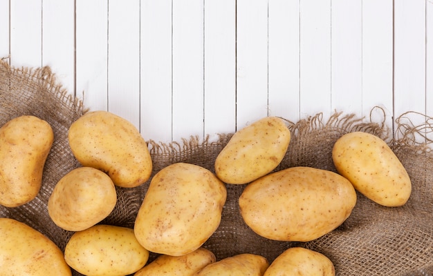 Raw potato, pile of potatoes on burlap on white wood