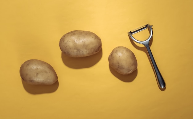 Сырой картофель и нож для очистки на желтом фоне. Вид сверху