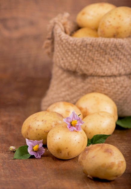 Сырой картофель с цветами в сумке на деревянном фоне