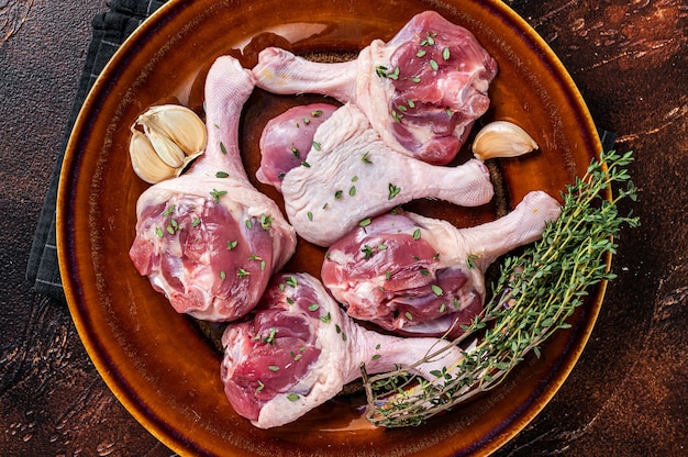 Carne cruda di pollame - cosce di cosce di anatra su un piatto rustico con erbe aromatiche. sfondo scuro. vista dall'alto.