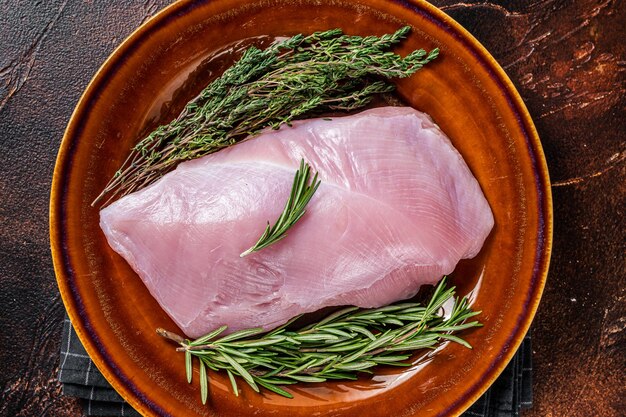 Raw Poultry turkey breast fillet meat in a rustic plate with rosemary and thyme. Dark background. Top View.