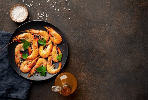Photo raw prawns in a black plate with herbs and spices on a stone background
