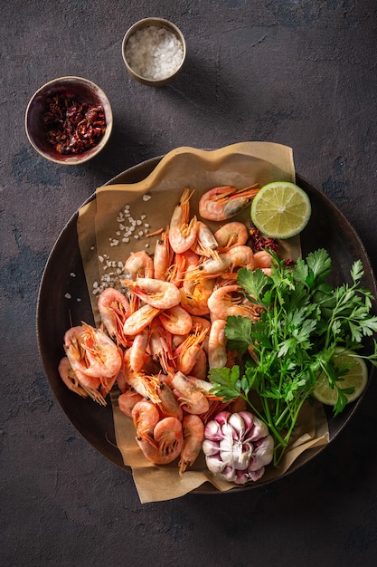 Raw prawns in a cooking pan with ingredients for preparation fried shrimps on a dark top view