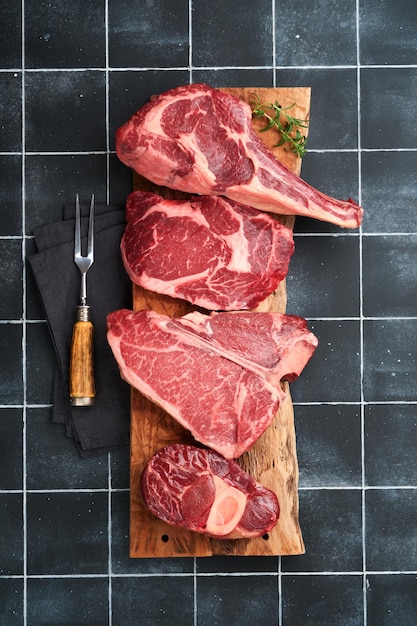 raw prime steaks variety of fresh black angus prime meat steaks tbone new york ribeye striploin tomahawk on black old tiles stone background set of various classic steaks top view copy space