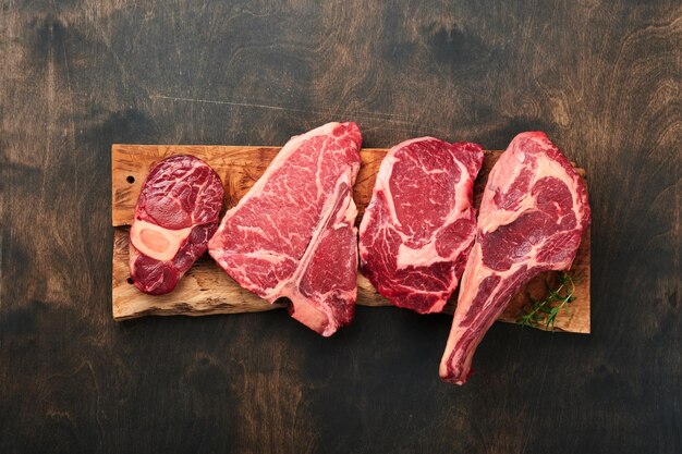 Raw prime steaks Variety of fresh black angus prime meat steaks Tbone New York Ribeye Striploin Tomahawk cutting board on black or dark background Set of various classic steaks Top view