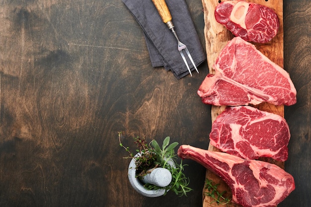 Raw prime steaks Variety of fresh black angus prime meat steaks Tbone New York Ribeye Striploin Tomahawk cutting board on black or dark background Set of various classic steaks Top view