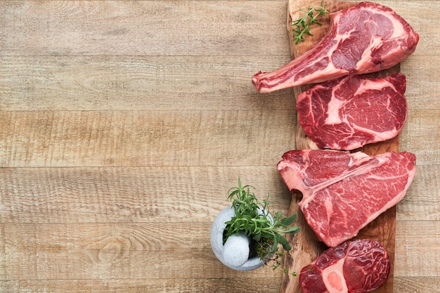 Raw prime steaks Variety of fresh black angus prime meat steaks Tbone New York Ribeye Striploin Tomahawk cutting board on old wooden background Set of various classic steaks Top view