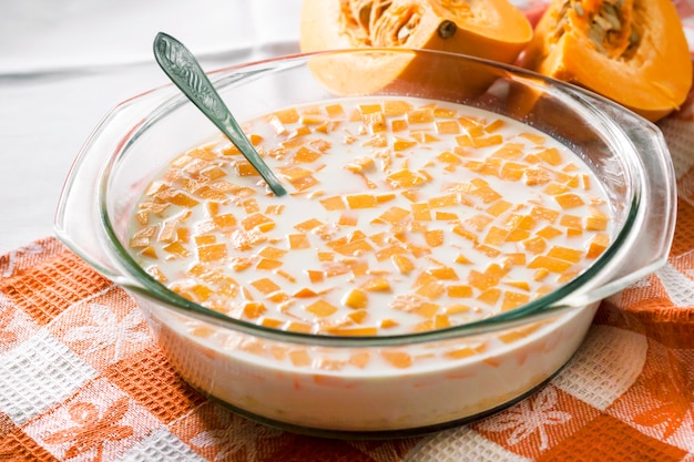 Raw pumpkin and milk in glass pan in the process of cooking pumpkin porridge with raising