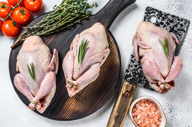 Raw quails preparation on a wooden cutting board with meat cleaver