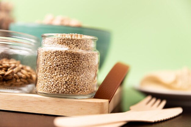 Raw quinoa in glass mini jar on rustic wooden table on green background